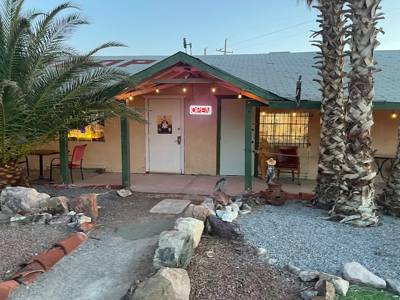 Storefront on the Old Spanish Trail Highway in Tecopa at dusk, with string lights, a glowing OPEN sign, and palm trees